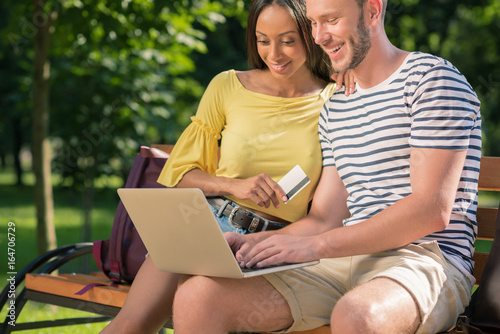 happy multiethnic couple shopping online with laptop and credit card while sitting on bench in park © LIGHTFIELD STUDIOS