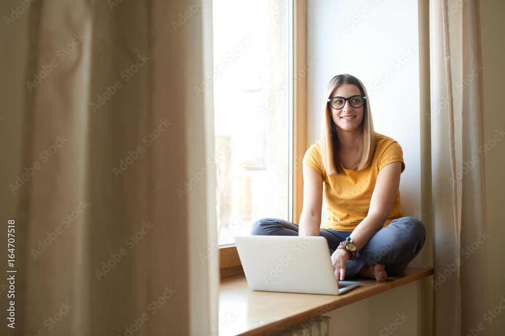 Charming woman working at the computer on the windowsill Charming woman working at the computer on the windowsill