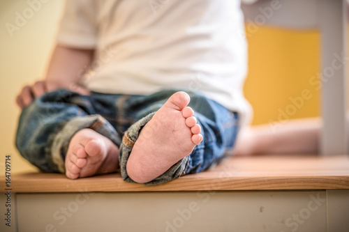  legs of a small child sitting on a chair close-up. Front focus.