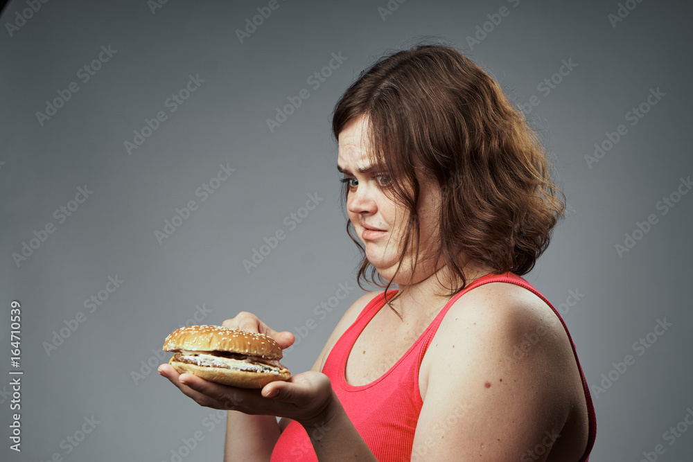 Fat woman on a gray background holds a hamburger Fat woman on a gray background holds a hamburger