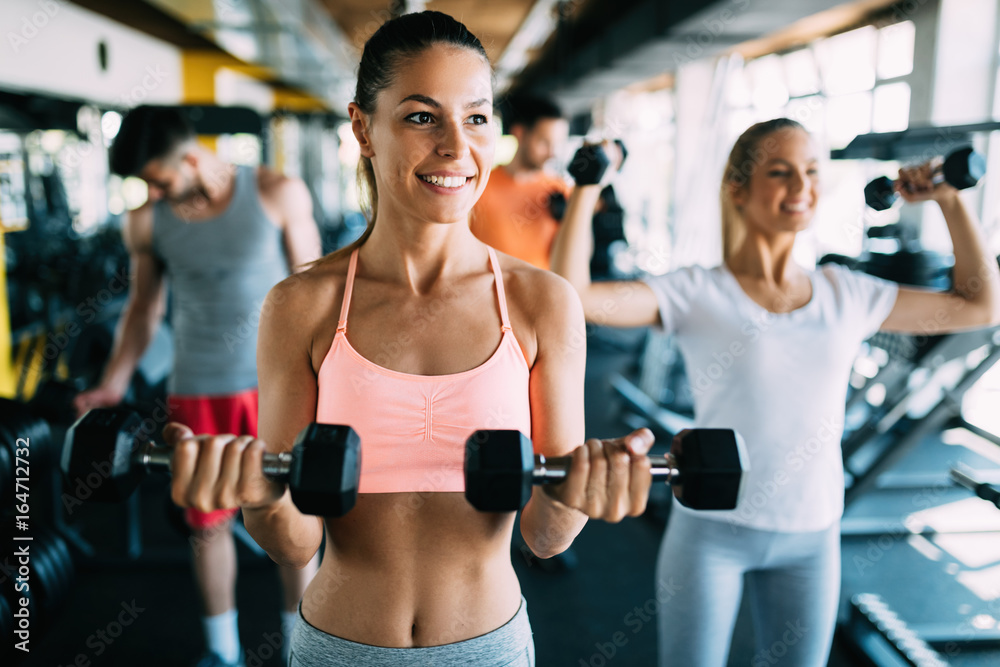 Young attractive woman with friends doing exercises in gym