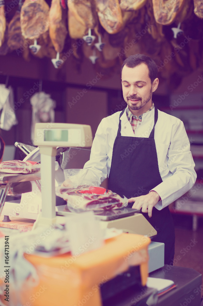 Fototapeta premium male seller weighing piece of meat in butcher’s shop