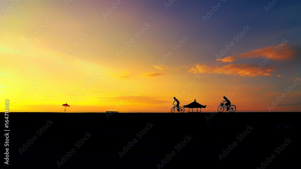 Young couple in love chasing each others on a bicycle during sunrise near Karang Beach Sanur Bali Indonesia. (blurry noise visible soft focus) Nature composition Young couple in love chasing each others on a bicycle during sunrise near Karang Beach Sanur Bali Indonesia. (blurry noise visible soft focus) Nature composition