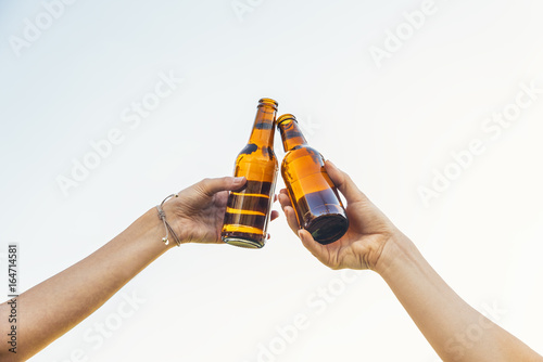 Fotografie Female friends cheers clinking bottles of beer in hands in the park