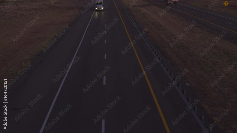AERIAL CLOSE UP: Cars and freight semi trucks loaded with goods driving along a busy highway, transporting cargo before dawn. Container truck delivery transporters hauling cargo at dusk after dark AERIAL CLOSE UP: Cars and freight semi trucks loaded with goods driving along a busy highway, transporting cargo before dawn. Container truck delivery transporters hauling cargo at dusk after dark