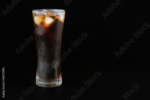 Cola water in a glass with ices over black background, industrial food and drink concepts.