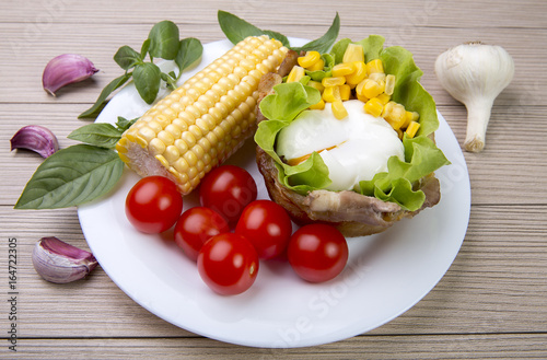 The poached egg in the basket of bacon with herbs and tomatoes and corn with garlic. On wooden background.