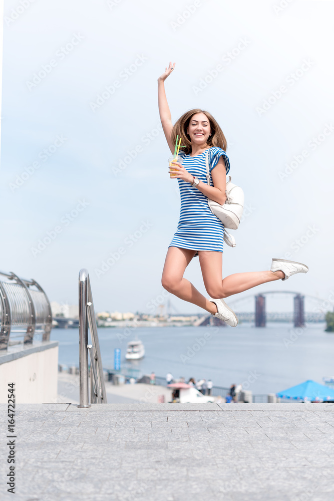 Pretty young woman drinking fruit cocktail and enjoying sun and good warm day near the river, summer vacation, woman relaxing outdoors.