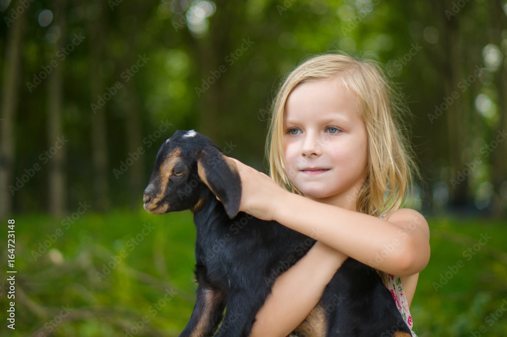 Adorable girl in park hold small beautiful baby goat