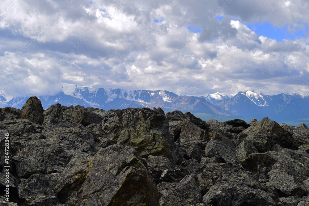 Stone run in Altai mountains, white clouds and snow peaks of North-Chuyski ridge. Aktash, Altay Republic, Siberia, Russia.