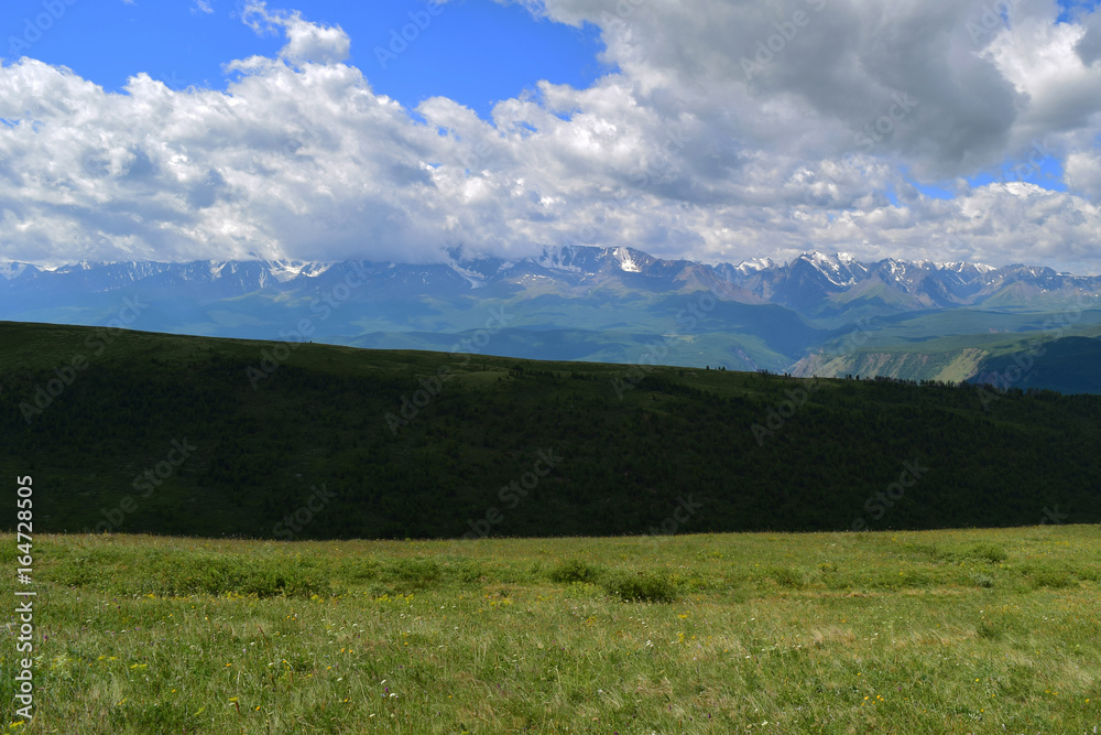 White peaks of North-Chuysky ridge and green field in Altai mountains. Aktash, Altay Region, Siberia, Russia.
