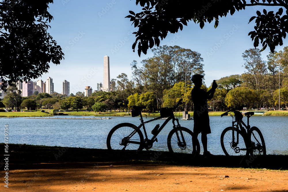 Fototapeta premium Cyclist by the lake in Ibirapuera Park, Sao Paulo, Brazil, taking photos.
