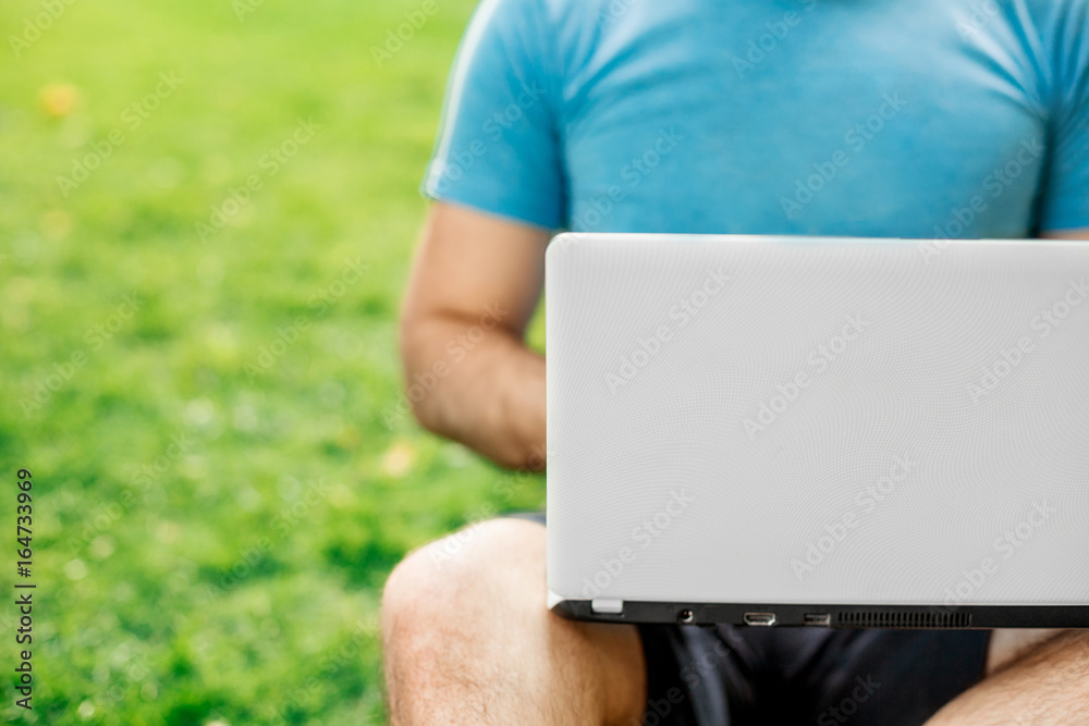 Naklejka premium Young man using and typing laptop computer in summer grass.
