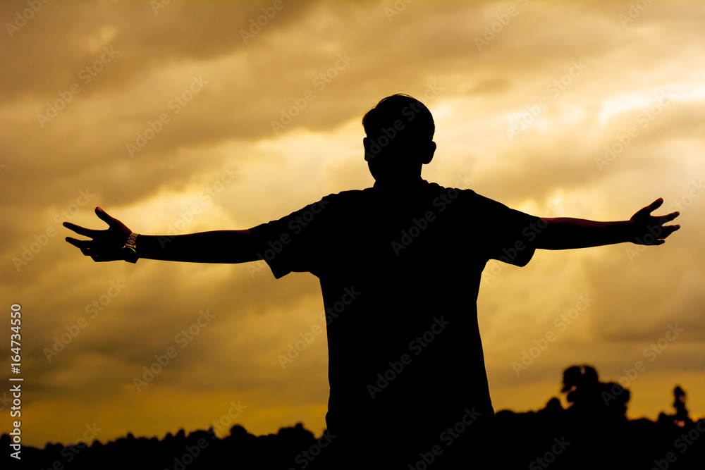 Silhouette man praying with hand up to God. Sunset background.