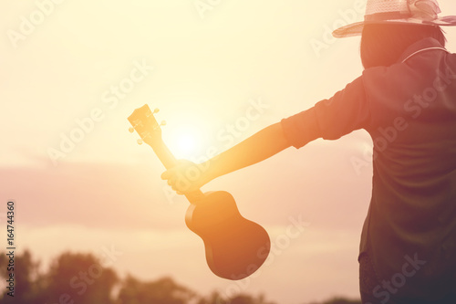 Woman holding ukulele and raise two arms embrace  summer sky with puffy clouds,