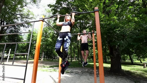 Young sportive woman and bearded man doing pull-ups exercises on crossbar in a parrk at summer day. photo