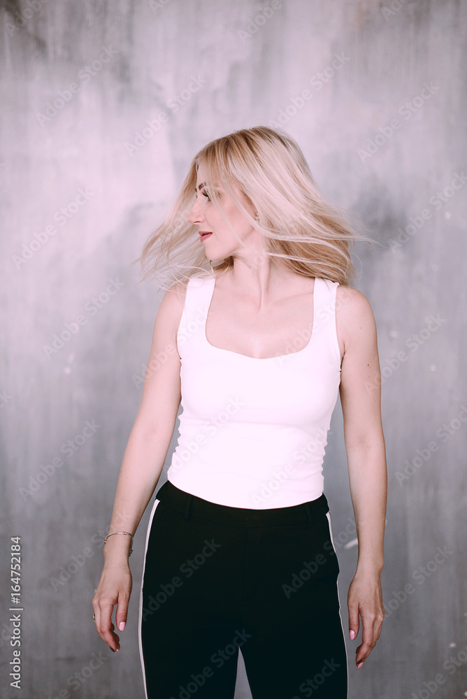 Fototapeta premium Attractive positive middle-aged blond woman wearing pink jacket and pants with trouser stripes with a beautiful smile posing against a receding wall looking directly at the camera. 