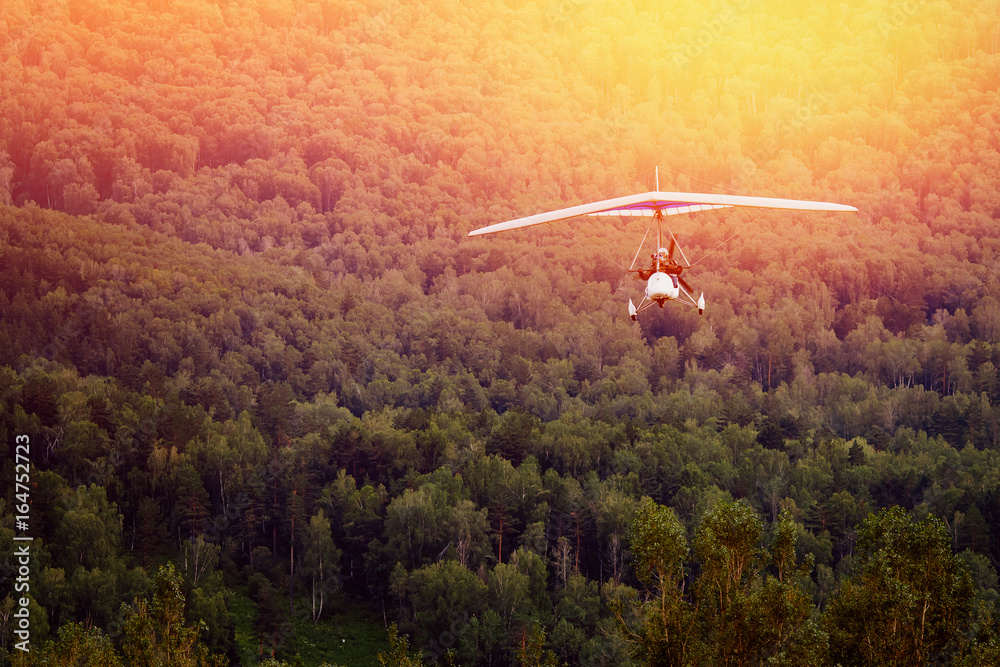 Fototapeta premium paraglider with a motor on the background of mountains and forests, in the setting sun, moves to the camera. The concept of extreme rest in the air.