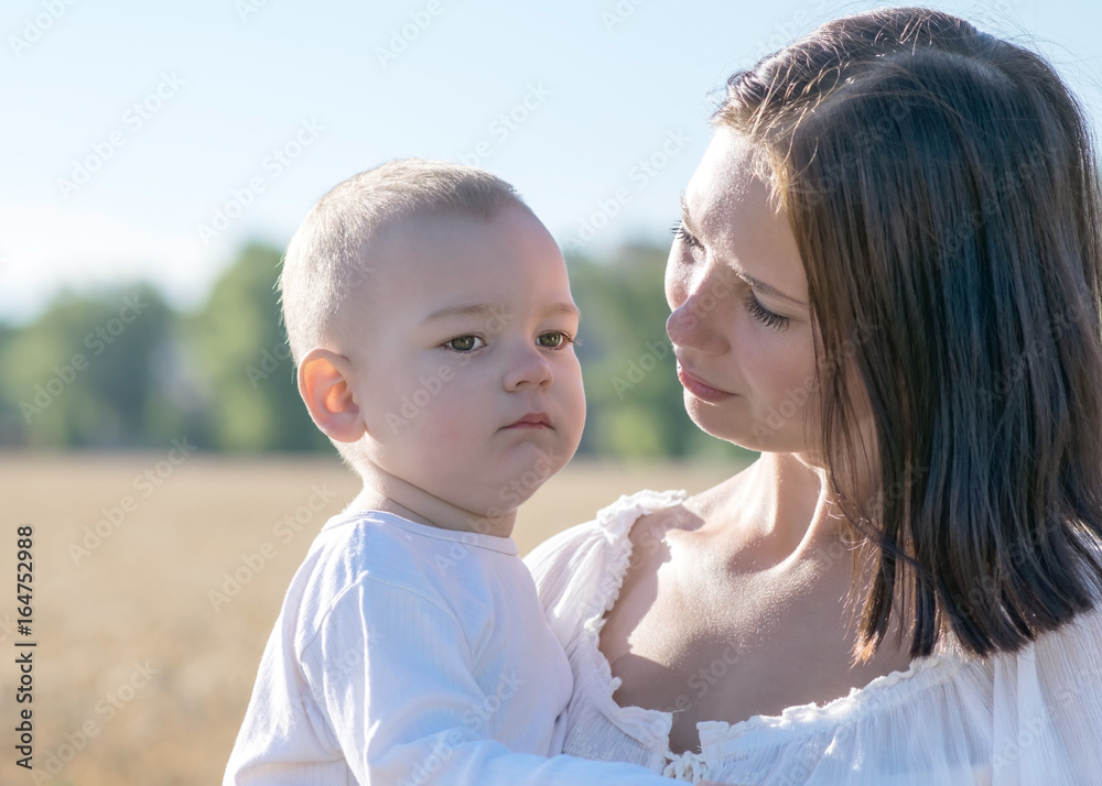 Fototapeta premium Young beautiful mother Holding child in her arms on nature in summer. Pretty woman looking with love on her baby son