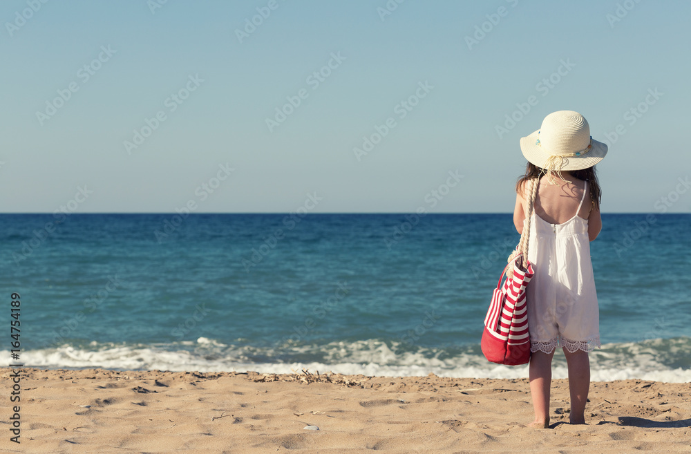 Little girl in white dress walking alone the sea, playing on the seashore