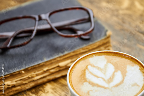 Coffee, old book and glasses. Latte with foam close up. Can coffee make you smarter.