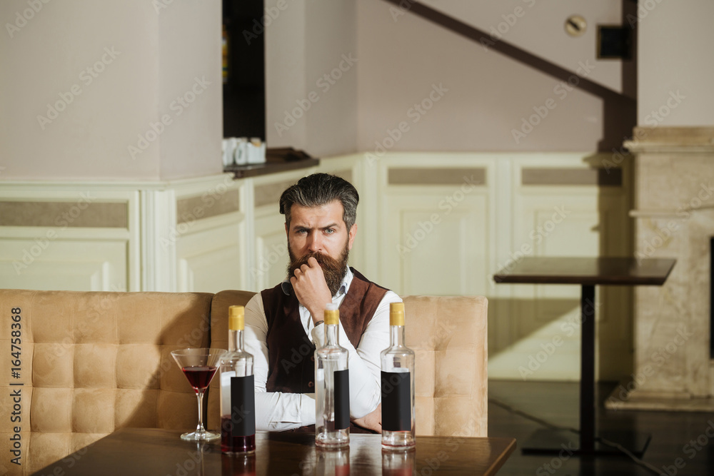Hipster sitting on sofa with martini glass and three bottles Hipster sitting on sofa with martini glass and three bottles