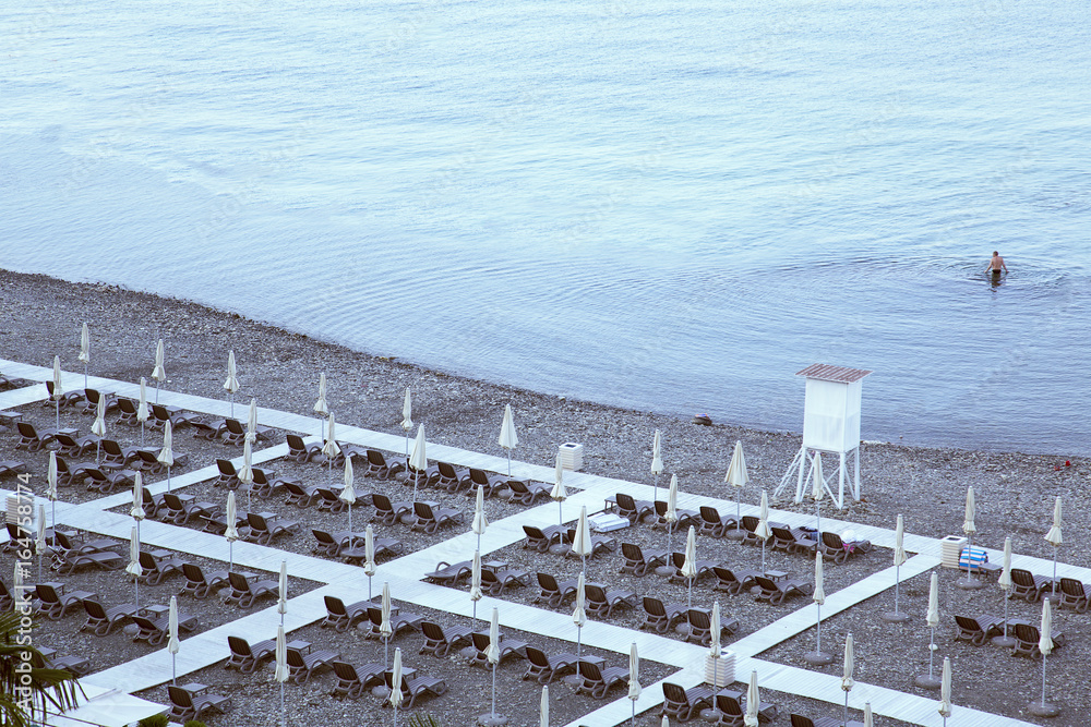 Beach umbrellas with deckchairs at the end of the summer season. One person is swimming in the sea. The beach season finished. Beach umbrellas with deckchairs at the end of the summer season. One person is swimming in the sea. The beach season finished.