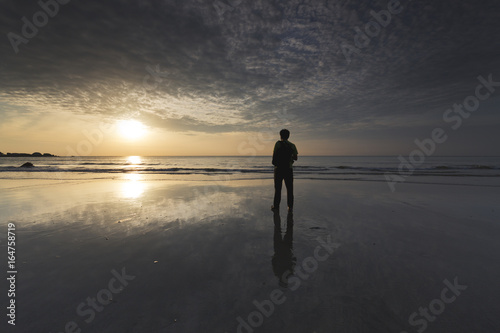 A silhouette of a man standing at the beach. His shadow was reflected on the sandy beach. This can be used as concept for travel as well as people expressing their emotion on future en devours. 