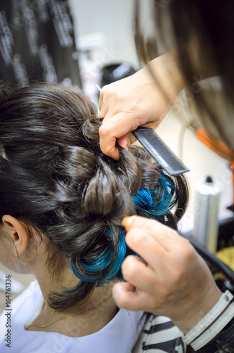 Closeup of a professional hairdresser's hands doing a hairstyle in a beauty salon. Model of a brunette with long hair. The concept of fashionable stylish hairstyle, professional work with hair.