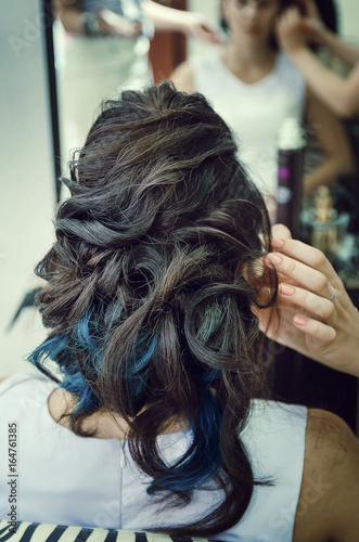 Closeup of a professional hairdresser's hands doing a hairstyle in a beauty salon. Model of a brunette with long hair. The concept of fashionable stylish hairstyle, professional work with hair.