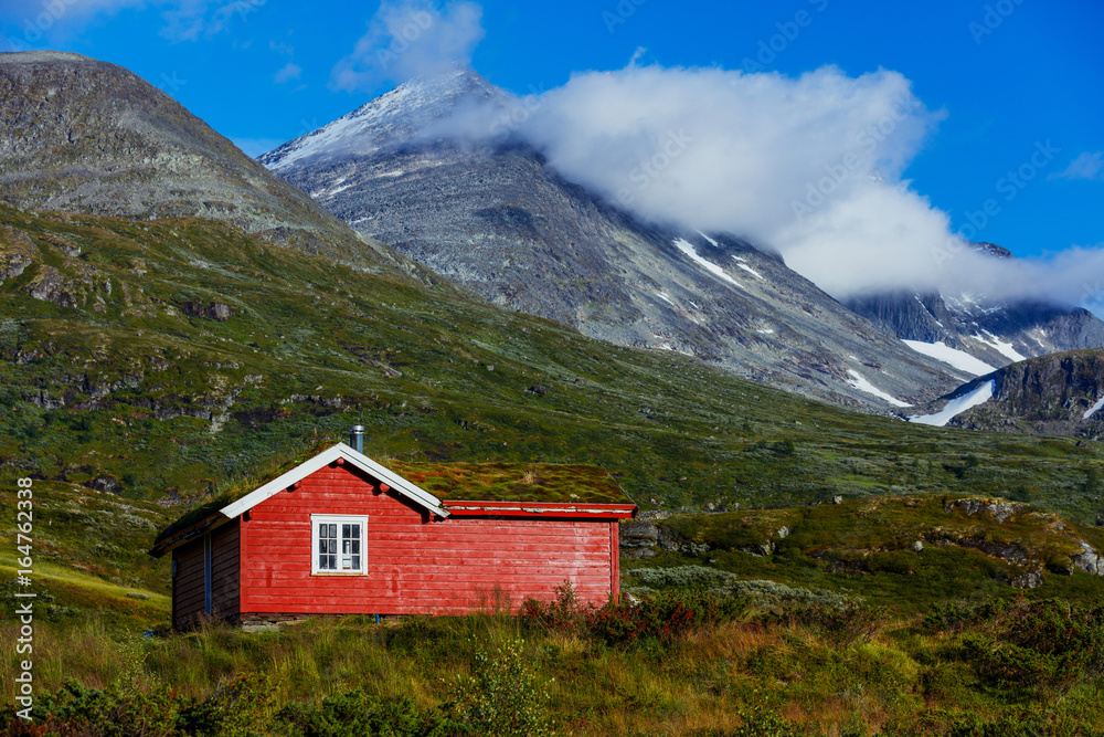 Wooden cottage in the valley. Stone snowy mountains. Norway.