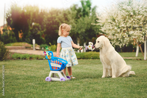 Little cute girl playing with big golden retriever in the garden at summer day