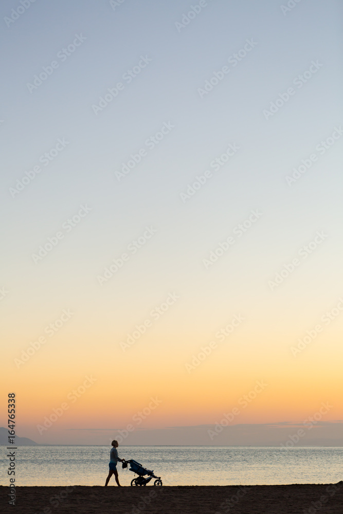 Obraz premium Silhouette of mother with stroller enjoying motherhood at sunset landscape