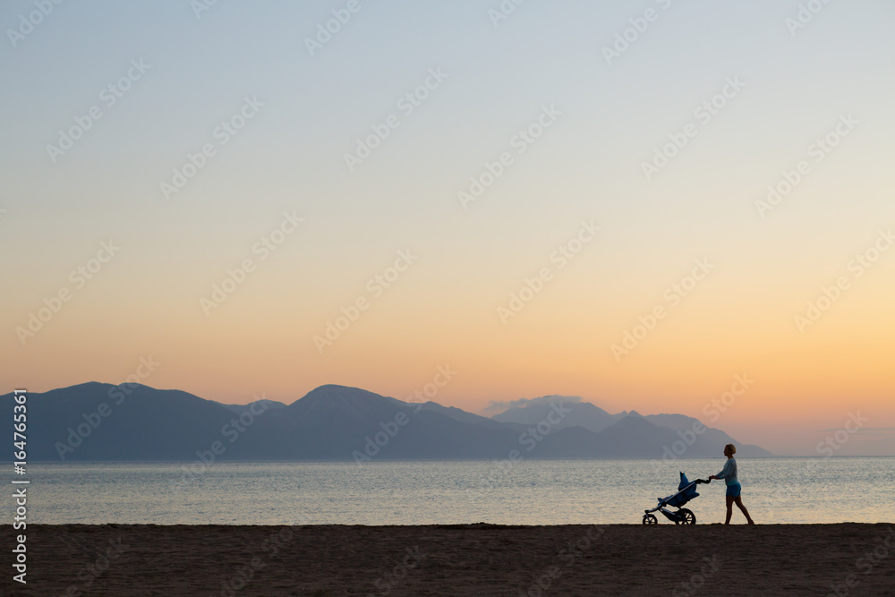 Silhouette of mother with stroller enjoying motherhood at sunset landscape