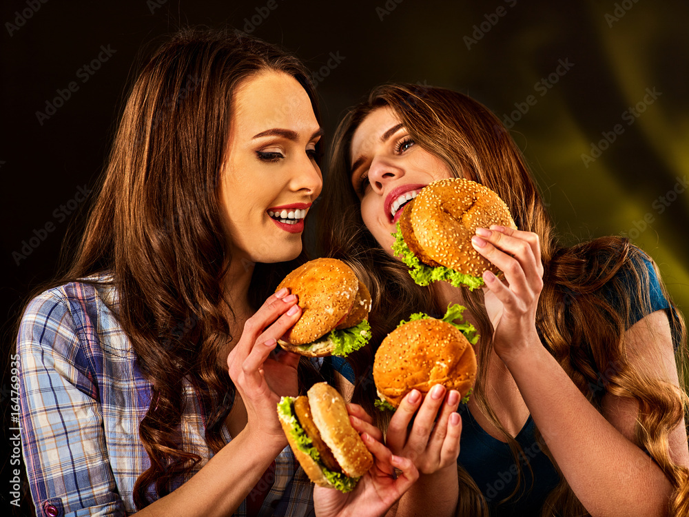 Hamburger fast food with ham and group people. Good Fast food concept. Friends two women eating sandwich junk in party. Girls eat up after diet.