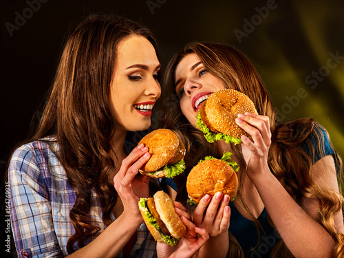 Hamburger fast food with ham and group people. Good Fast food concept. Friends two women eating sandwich junk in party. Girls eat up after diet.