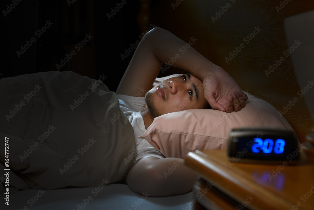 Depressed man suffering from insomnia lying in bed - obrazy, fototapety, plakaty 