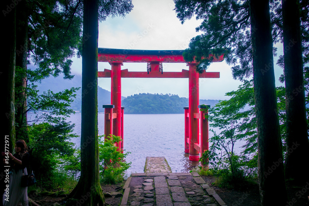 Bright red Torii gate submerged in the waters of Ashi lake, caldera with mountains on the background. Hakone Shrine, Kanagawa prefecture, Japan Bright red Torii gate submerged in the waters of Ashi lake, caldera with mountains on the background. Hakone Shrine, Kanagawa prefecture, Japan