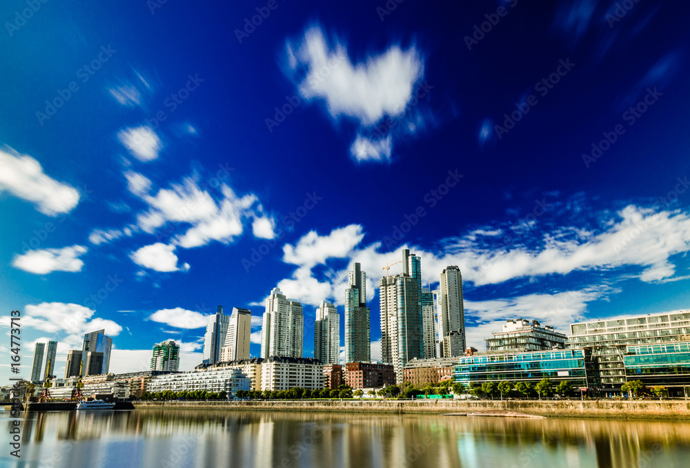 Long exposure photo of skyscrapers in Puerto Madero business district in Buenos Aires against colorful blue sky with clouds on a sunny day. Wide angle, heavy polarizer filter.