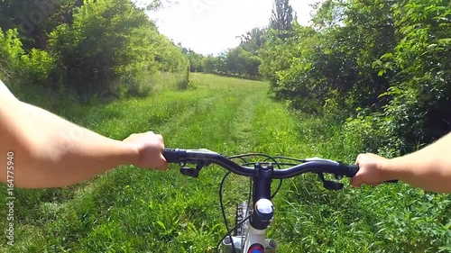 Cyclist girl riding a bicycle in a green forest on an earthen path on a sunny summer day. Action camera go pro. Caucasian