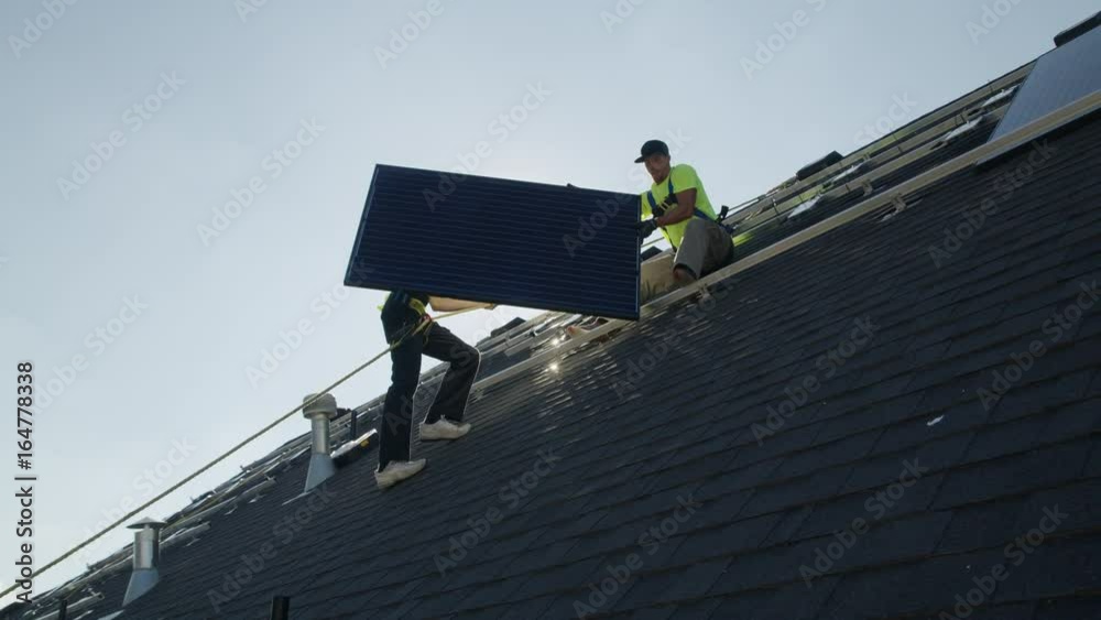 Wide panning low angle shot of workers carrying solar panel on roof / Mapleton, Utah, United States