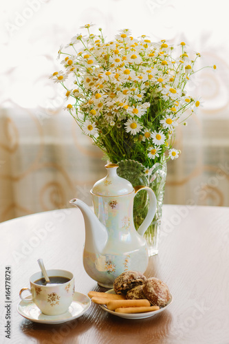 Morning coffee. Hot coffee Cup coffee pot and a bouquet of daisies in vase on wooden table on window background.