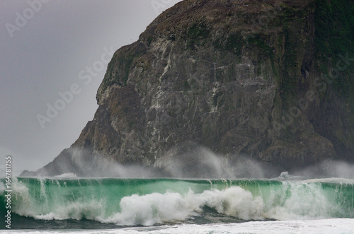 Wave crashes in front of large rock (monolith) during Winter storm on Oregon Coast.