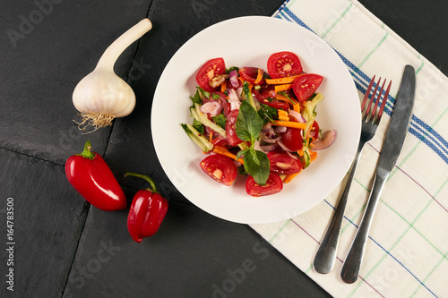Top view of a vegan summer salad on black stone background. Fresh vegetables salad with mixed greens and cherry tomato сarrot cucumber bell pepper red onion in white plate. Healthy vegetarian food