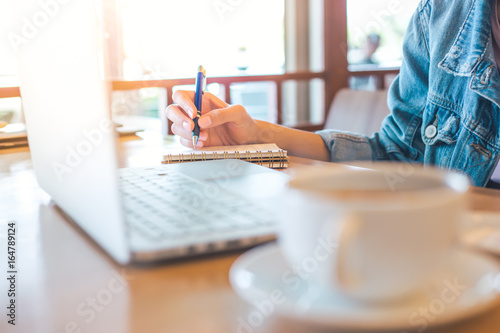 woman's hand using laptop and writing in notepad.Soft focus