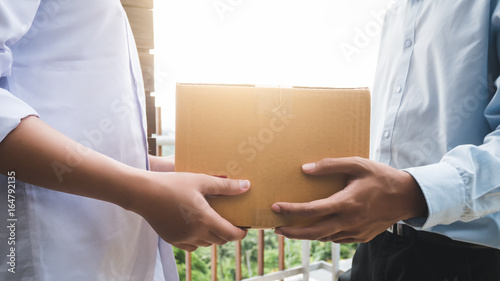 Close up hand of asia woman are receive a box from delivery man with sun light in delivery service concept.