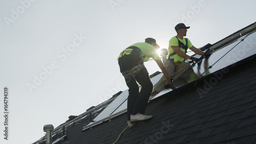 Medium panning low angle shot of workers installing solar panel on roof / Mapleton, Utah, United States
