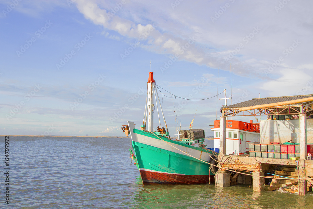 The green fishing boat is whitewashed against the pier with blue sky.
