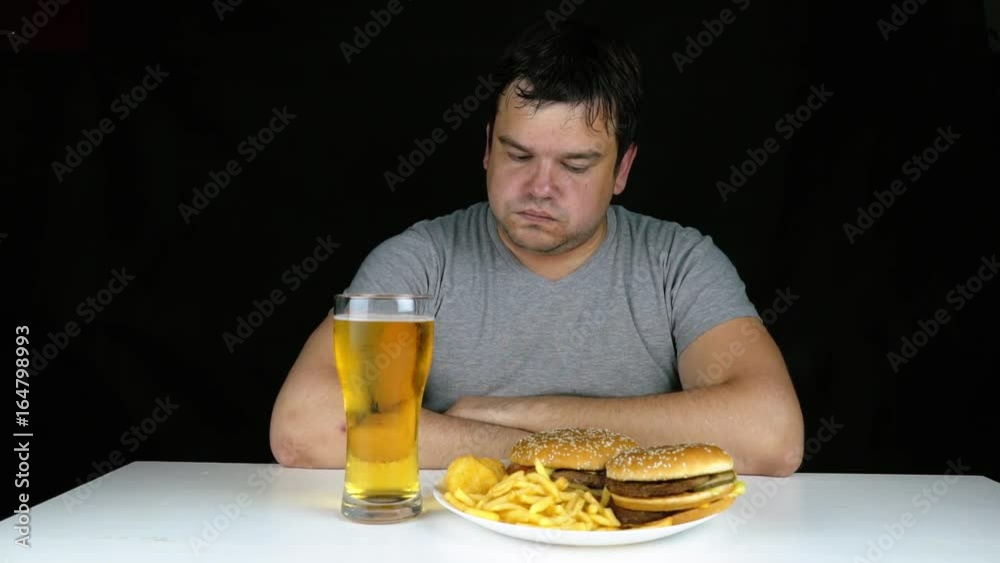 Diet failure of fat man eating fast food hamberger. Happy smile overweight person who spoiled healthy food by eating huge hamburger on fork. Junk meal leads to obesity. Refusal from harmful food. Diet failure of fat man eating fast food hamberger. Happy smile overweight person who spoiled healthy food by eating huge hamburger on fork. Junk meal leads to obesity. Refusal from harmful food.