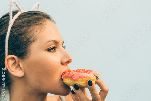 Close up of sexy slim woman eat tasty sweet heart shaped donut. Beauty cute girl in a tropical resort. Outdoor lifestyle portrait on hot sunny summer day. Concept of love, feelings, positive emotions.